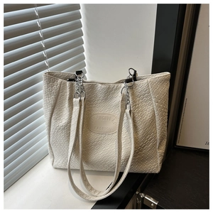 Detail of creamy white tote bag featuring faux crocodile texture and chain strap