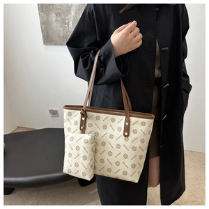Detail of large beige tote bag with brown leather straps shown on a model in a black coat