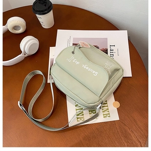 Detail of light green canvas crossbody bag with sausage dog print and plush keychain