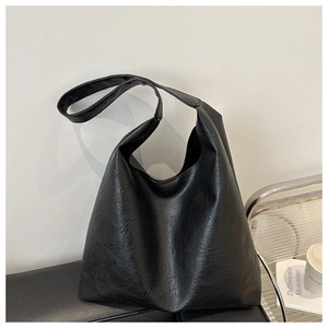 Detail of black pebbled leather tote bag with wide strap on a modern chair