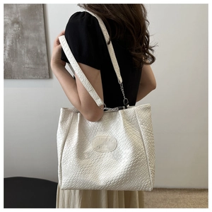 Detail of white woven tote bag with silver chain strap and logo patch on model