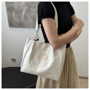 Detail of white quilted tote bag with chain strap and leather logo tag on shoulder