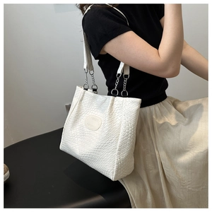 Detail of white woven tote bag featuring silver chain strap and fashion embossed patch