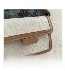 Detail shot of white faux leather crossbody bag with brown trim and crocodile texture