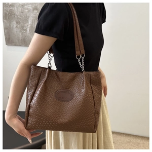 Detail of brown woven tote bag showing leather logo patch and silver chain strap
