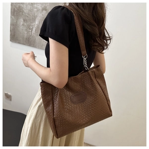 Detail of brown woven texture tote bag featuring metallic chain strap and logo patch