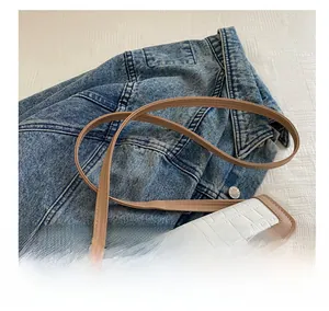 Detail showing contrast stitching and crocodile texture of the crossbody bag on denim