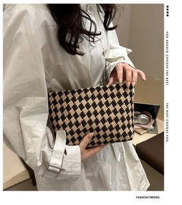 Close-up of a stylish woven checkered clutch bag held in a modern office environment