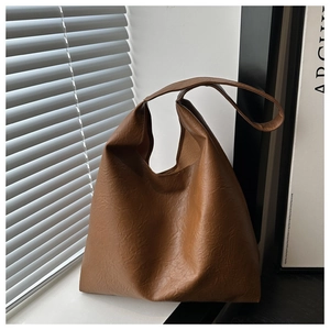 Macro shot of brown leather tote bag showing detailed natural wrinkled texture and wide strap