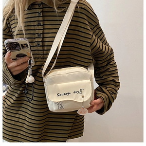 Detail shot of a cream canvas crossbody bag with a cute sausage dog print and wide strap