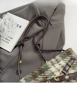 Détail du sac seau en tweed montrant la texture à carreaux verts et la bandoulière en cuir