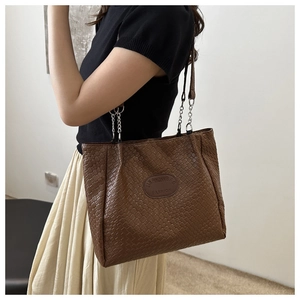 Detail of deep brown woven quilted tote bag featuring a round logo and chain strap