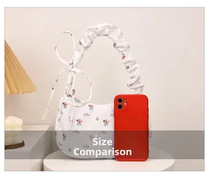 Size comparison of white floral crescent bag next to a smartphone showing compact dimensions