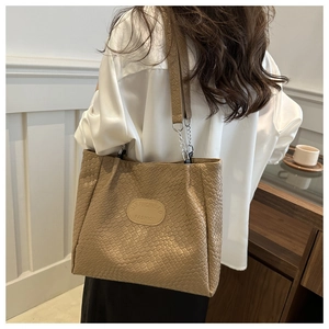 Detail of brown woven texture tote bag with chain strap and metallic brand emblem