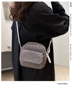 Détail d'un sac à bandoulière en toile grise à motifs de cœurs rouges porté par un mannequin