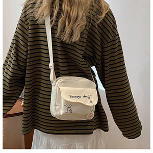 Detail of a beige canvas crossbody bag with a cute sausage dog print and cartoon zipper puller
