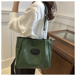 Detail of dark green quilted tote bag with chain strap and brand logo patch