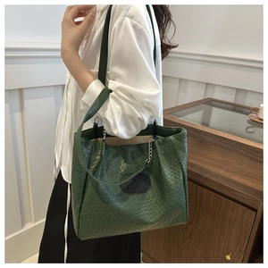Detail of dark green woven tote bag featuring an oval blue brand patch and chain strap