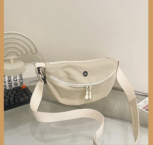Detail of beige crescent canvas bag with dual zippers and wide woven shoulder strap
