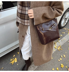 Détail d'un sac seau marron foncé brillant avec boucles dorées sur fond de rue d'automne