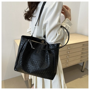 Detailed macro view of black quilted leather texture and logo plaque on tote bag