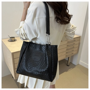 Detail of black woven texture tote bag with chain strap and logo patch for office wear
