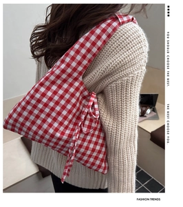 Detail of red checkered tote bag with side bow ribbon decoration on a knit sweater