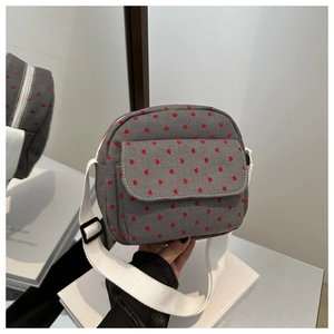 Détail du sac bandoulière en toile grise avec motifs cœurs rouges et sangle