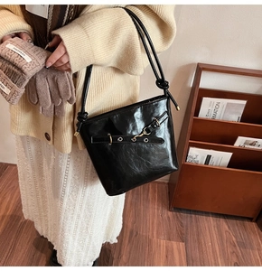 Détail d'un sac seau en cuir verni noir avec boucle dorée rétro et bandoulière élégante