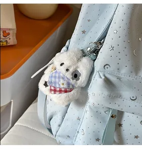 Close-up of a white plush puppy charm with scarf attached to a blue star pattern backpack