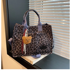 Detail of leopard print tote bag with plush bear charm on a white book by a window