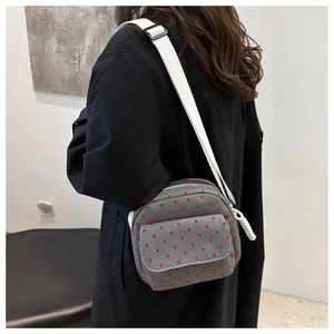 Détail du sac bandoulière en toile grise avec motif coeur rouge et sangle blanche