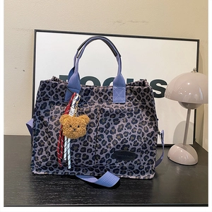 Detail of purple leopard print tote bag with front pockets and plush bear charm accent