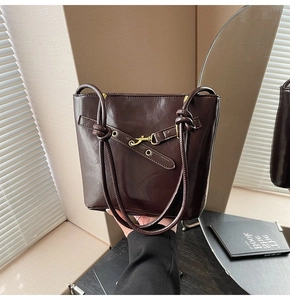 Détail du sac à bandoulière en cuir brillant marron foncé avec crochet doré et bandoulière