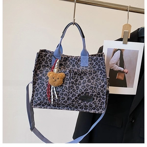 Detail of leopard print tote bag featuring blue straps, front pockets and cute bear charm