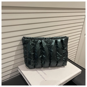 Detail of a dark green quilted puffy clutch bag placed on a book with soft lighting