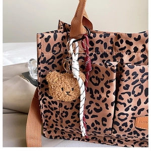 Detail of leopard print tote bag featuring a plush bear charm and woven rope decoration