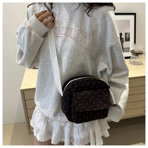 Gros plan du sac noir avec motifs de cœurs rouges et bandoulière blanche réglable