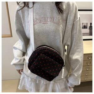 Détail d'un sac bandoulière en toile noire à motifs cœurs rouges et sangle blanche