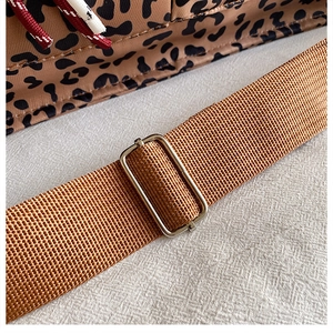 Detail of leopard print tote featuring a brown woven strap and silver metal buckle