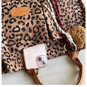 Detail of leopard print tote bag showing leather tag and pink phone in front pocket