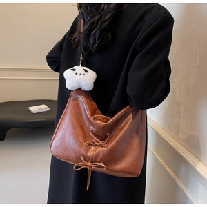 Dettaglio di una borsa tote in pelle marrone con ciondolo a stella e nappe con lacci decorativi