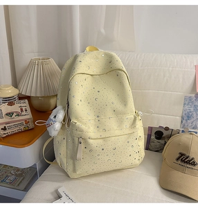 Detail of light yellow star-patterned backpack with plush pendant in cozy room setting