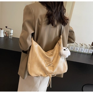 Dettaglio di una borsa tote beige con allacciatura incrociata e ciondolo panda in peluche