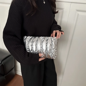 Silver puffy quilted clutch bag held by a model wearing a black turtleneck sweater