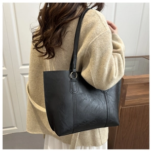 Detail of a black leather tote bag with gold rings shown on a shoulder in a home setting