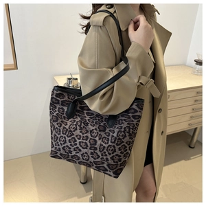 Detail view of large leopard print tote bag with black leather straps on a trench coat model