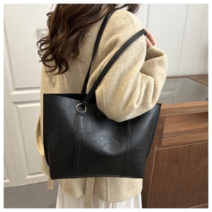 Detail of black tote bag with vintage leather texture and gold ring strap accents