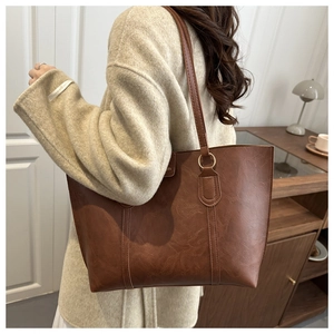 Close-up of dark brown lychee leather tote bag with gold metal rings and shoulder strap