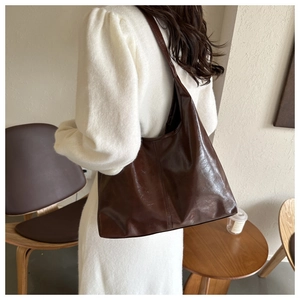 Deep brown glossy leather tote bag shown on shoulder in minimalist interior scene